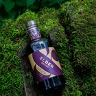 A bottle of Wild & Wonder Elder Berry liqueur resting on a mossy woodland background
