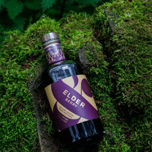 A bottle of Wild & Wonder Elder Berry liqueur resting on a mossy woodland background