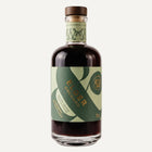 A bottle of Elder Orchard liqueur with a dark amber liquid, featuring a green and light green label with gold lettering and a brown wooden cap, set against a plain light grey background.