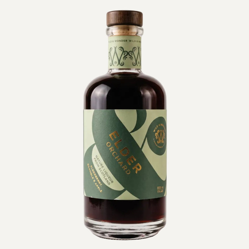 A bottle of Elder Orchard liqueur with a dark amber liquid, featuring a green and light green label with gold lettering and a brown wooden cap, set against a plain light grey background.