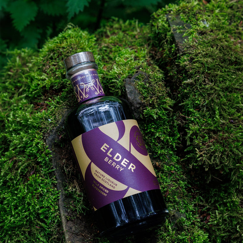 A bottle of Wild & Wonder Elder Berry liqueur resting on a mossy woodland background