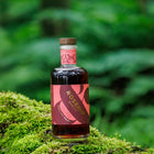 A bottle of Rosehip Spritz liqueur placed on a mossy log with a blurred green forest background.
