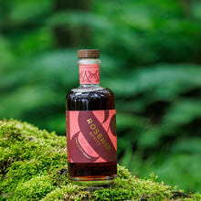 A bottle of Rosehip Spritz liqueur placed on a mossy log with a blurred green forest background.