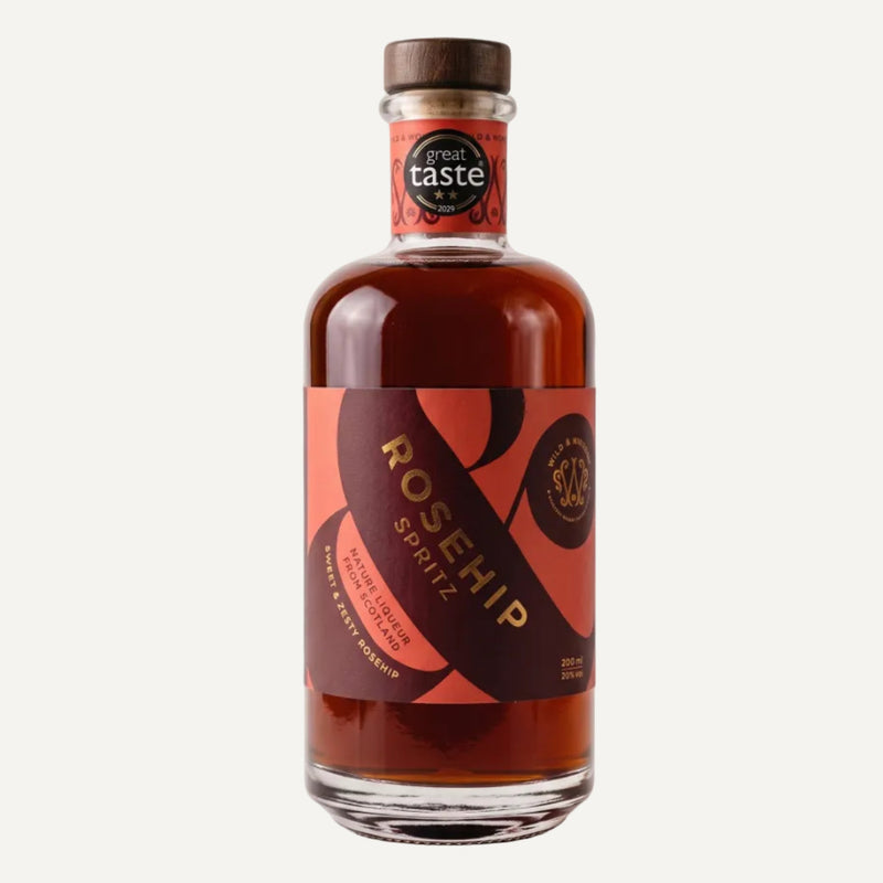 Bottle of Rosehip Spritz liqueur by Wild & Wonder. The bottle contains an amber liquid with a pink and dark red label with goild foil details and a dark brown wooden stopper