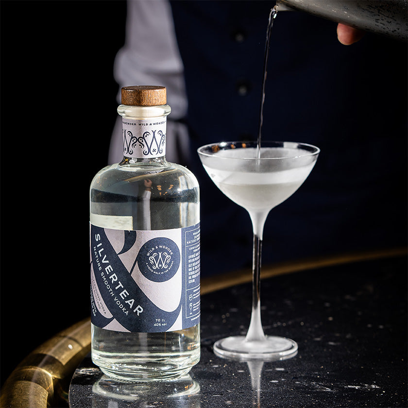 A bartender pours a Silvertear Nature vodka martini into a coupe glass beside the bottle