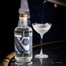 A bartender pours a Silvertear Nature vodka martini into a coupe glass beside the bottle