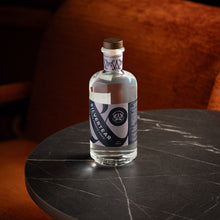A bottle of Silvertear Nature smooth birch sap vodka on a round black marble bar table, with a rust-orange velvet armchair behind it in a dimly lit bar.