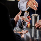 A guest holds a bottle of Silvertear Nature vodka at the bar while a bartender stirs a drink in a steel mixing tin.