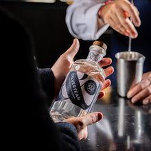 A guest holds a bottle of Silvertear Nature vodka at the bar while a bartender stirs a drink in a steel mixing tin.