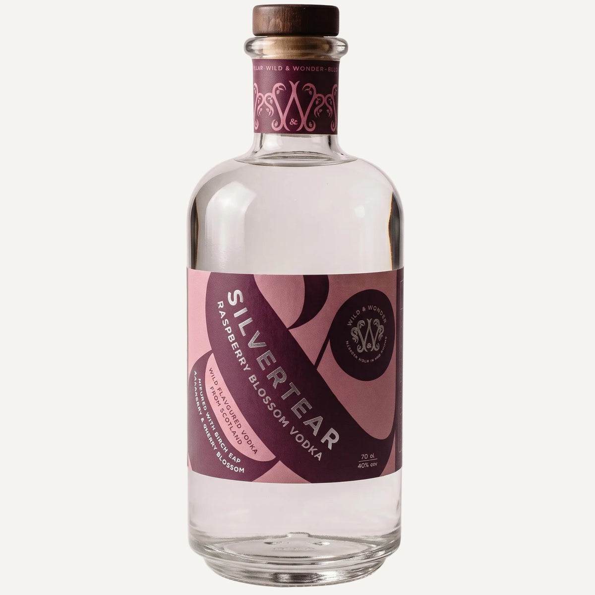 A bottle of Silvertear Raspberry Blossom Vodka on a light gray background. The clear glass bottle features a dark brown wooden cap, a purple and pink label with white text, and a matching purple neck label with a white monogram logo.