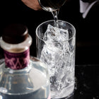 A bartender pours Silvertear Raspberry Blossom vodka over ice in a mixing glass, with the bottle in the foreground on a black marble bar.
