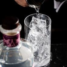 A bartender pours Silvertear Raspberry Blossom vodka over ice in a mixing glass, with the bottle in the foreground on a black marble bar.
