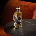 A bottle of Silvertear Vintage birch sap vodka, golden in colour with its Great Taste tag, on a round black marble bar table with a rust-orange velvet armchair behind it.