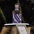 A bottle of Silvertear Nature smooth vodka displayed on rustic birch plinth with ring light, with a framed label in the foreground and a dark, blurred natural background.