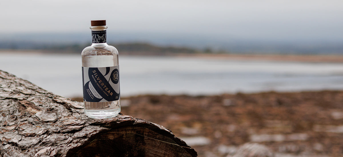 A bottle of Silvertear Nature vodka on a driftwood log by the sea