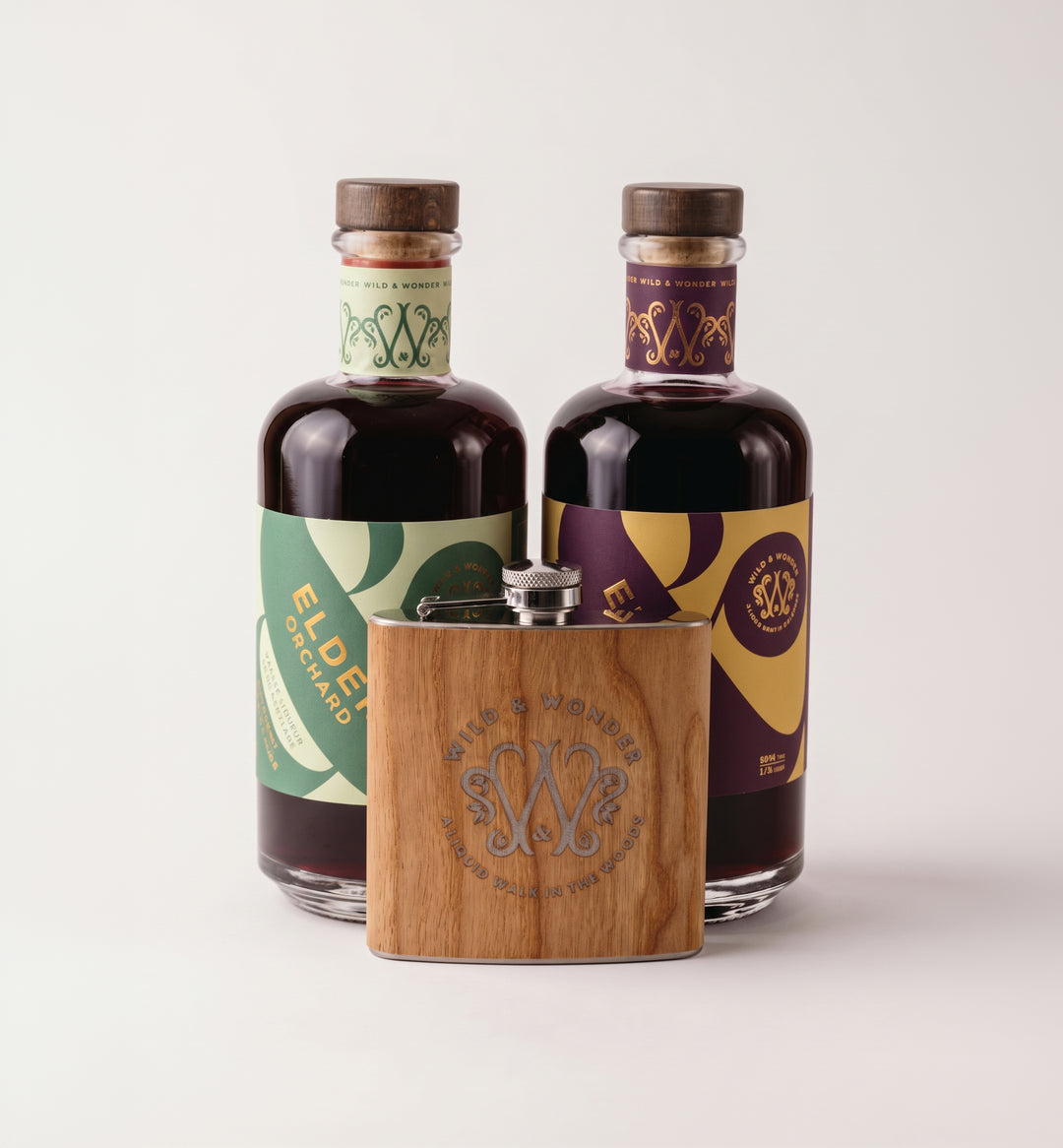 Bottles of Elder Orchard and Elder Berry liqueur with the wood-wrapped Wild & Wonder hipflask in front