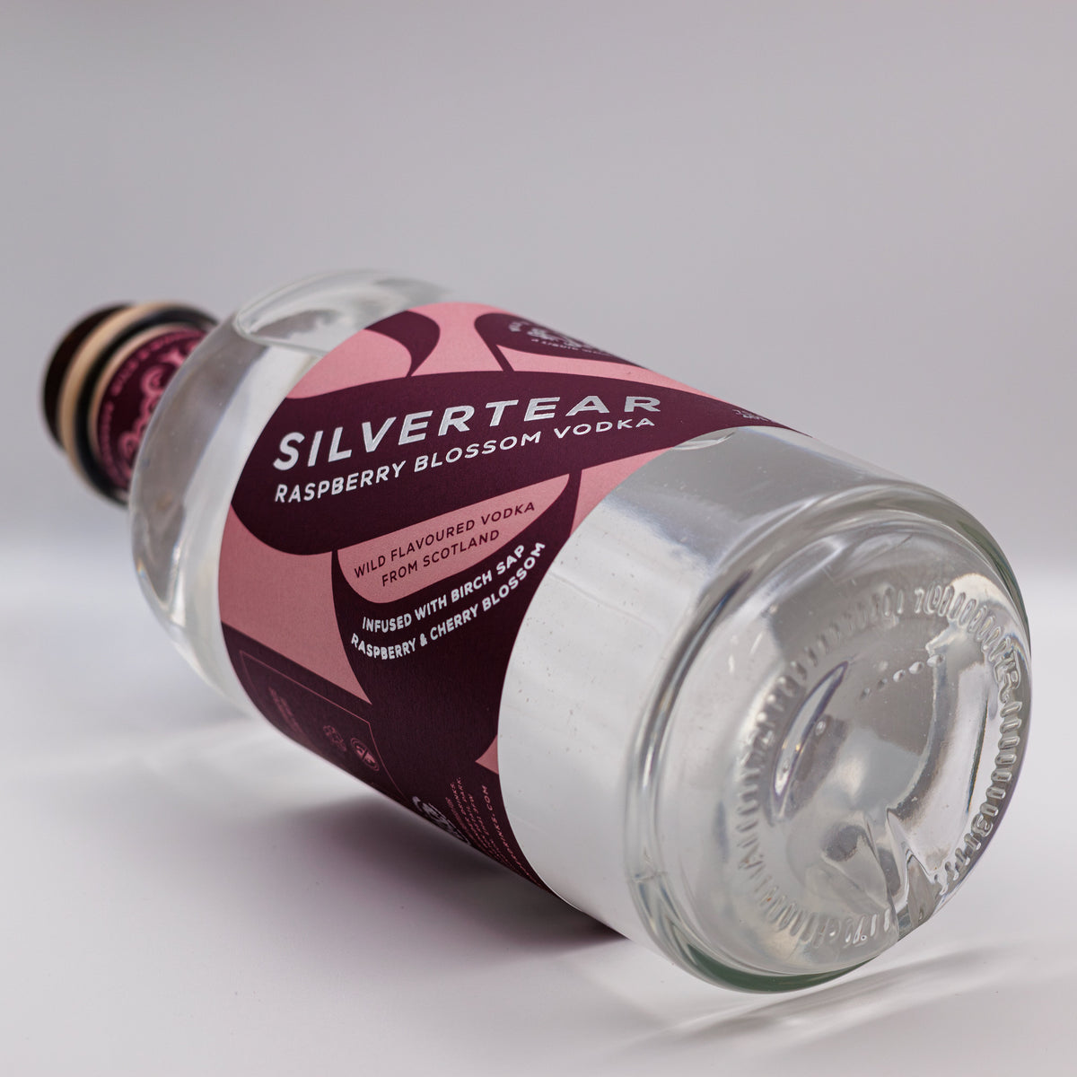 A bottle of Silvertear Raspberry Blossom vodka lying on its side on a white background