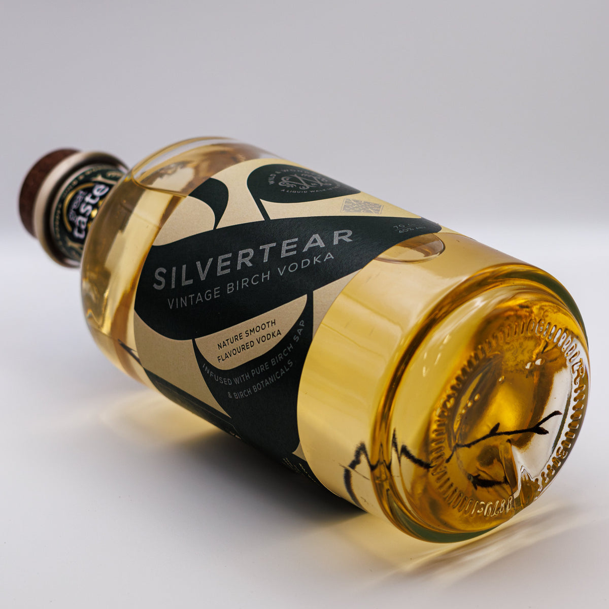 A bottle of golden Silvertear Vintage vodka lying on its side on a white background
