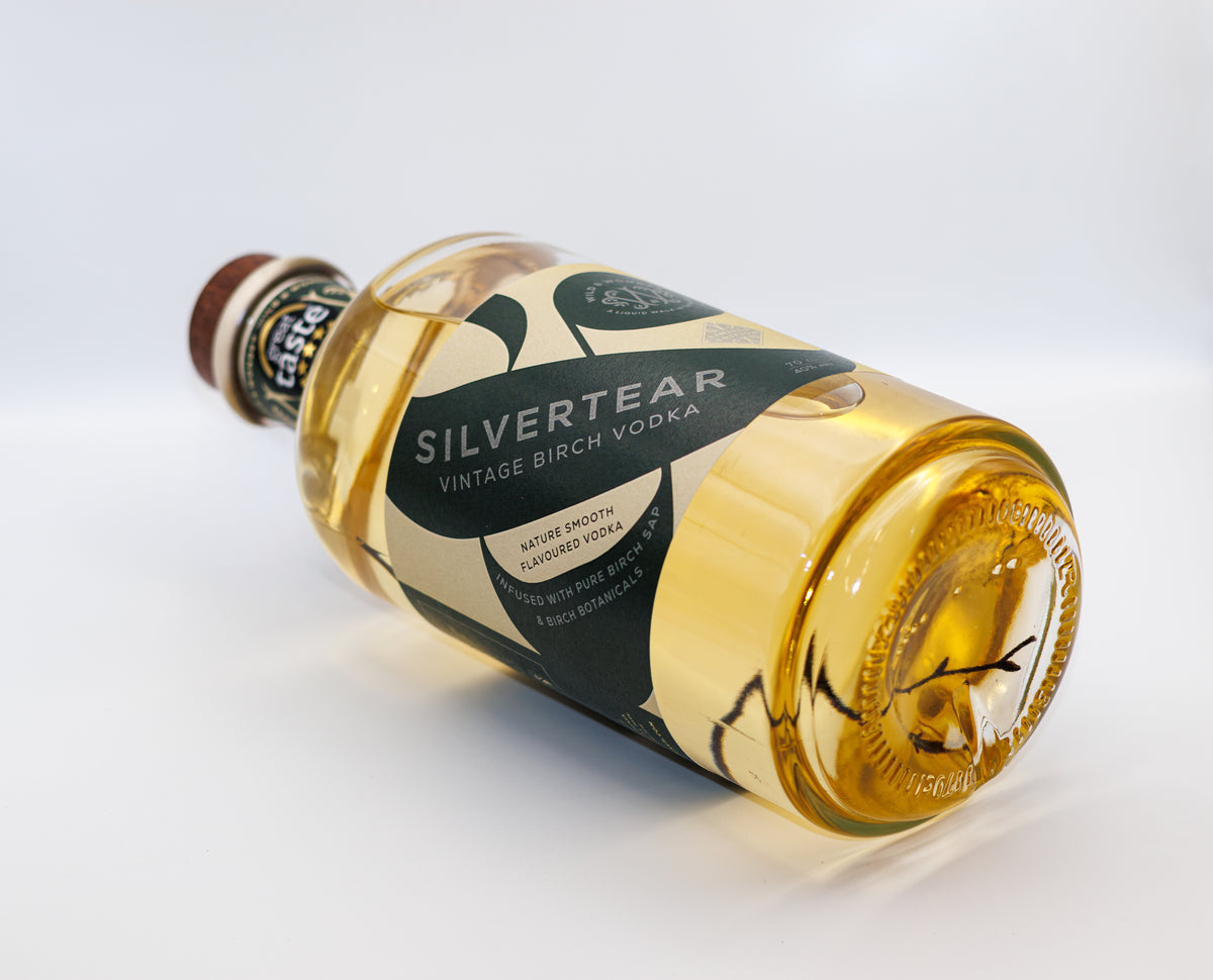 A bottle of golden Silvertear Vintage birch sap vodka lying on its side on a white background