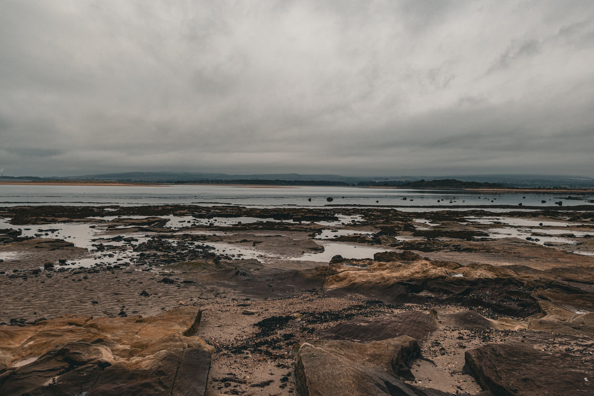 A wide rocky shoreline at low tide under a grey sky