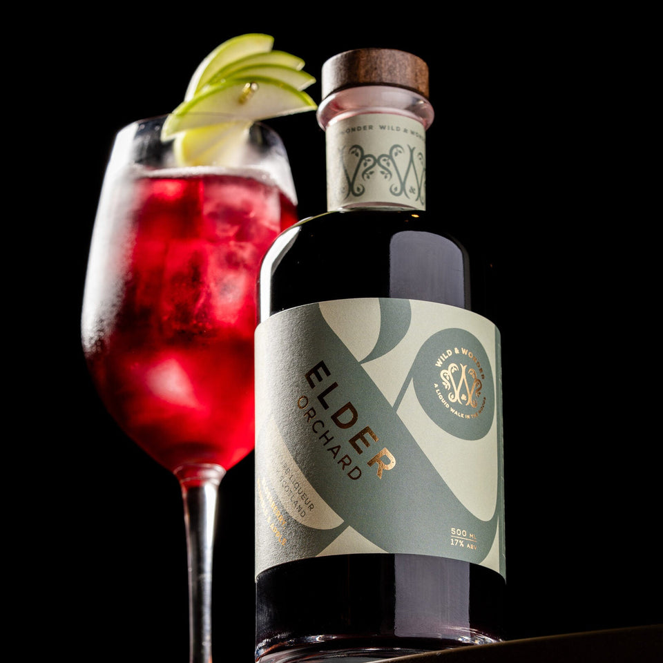 A Dark Berry Spritz with an apple garnish beside a bottle of Elder Orchard