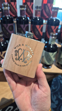 A hand holding the wood-wrapped Wild & Wonder hipflask at a tasting stand