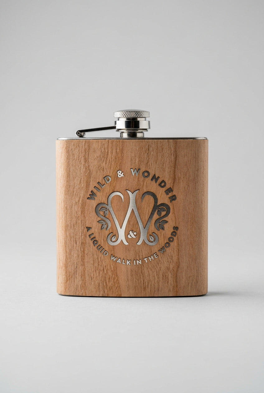 Wild & Wonder wood-wrapped stainless steel hipflask with engraved logo, on a grey background